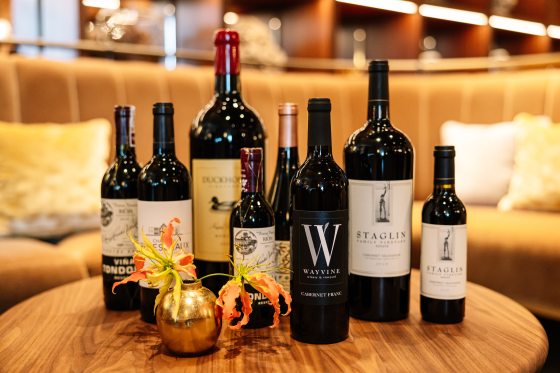 Eight bottles of wine, in different varieties, displayed on a small wood table. 